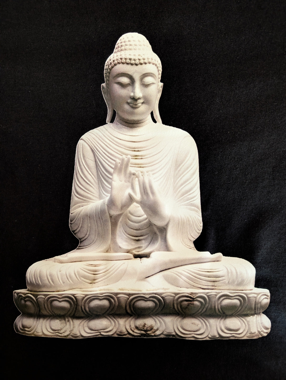 A white seated Buddha statue with a lotus base, photographed against a black fabric background.